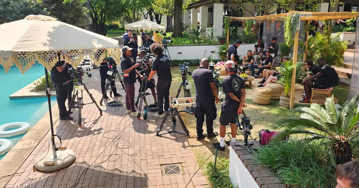 Multi-camera crew filming a cast interview on an outdoor reality TV set beside a pool